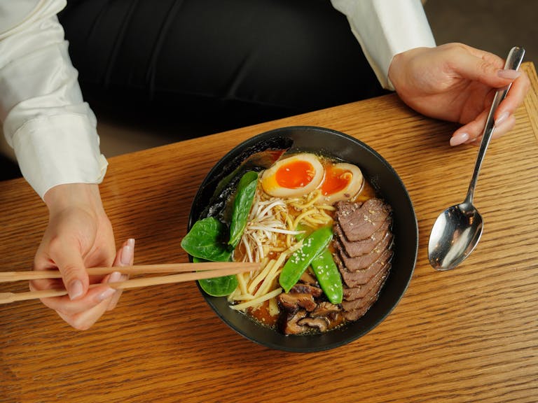 Close-up of a delicious ramen bowl with chopsticks and spoon on a wooden table.