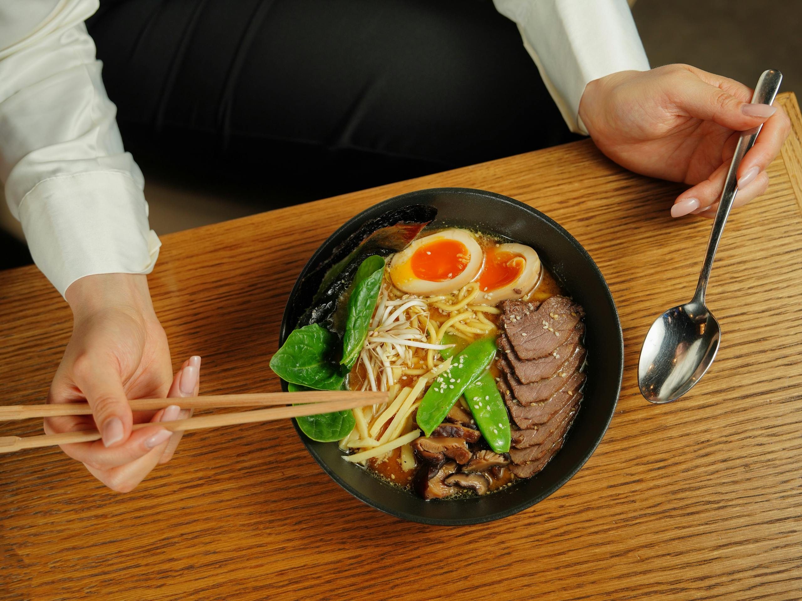 Close-up of a delicious ramen bowl with chopsticks and spoon on a wooden table.