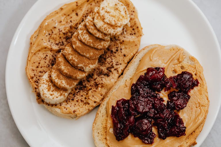 Close-up of peanut butter toast with banana and jam toppings on a plate.