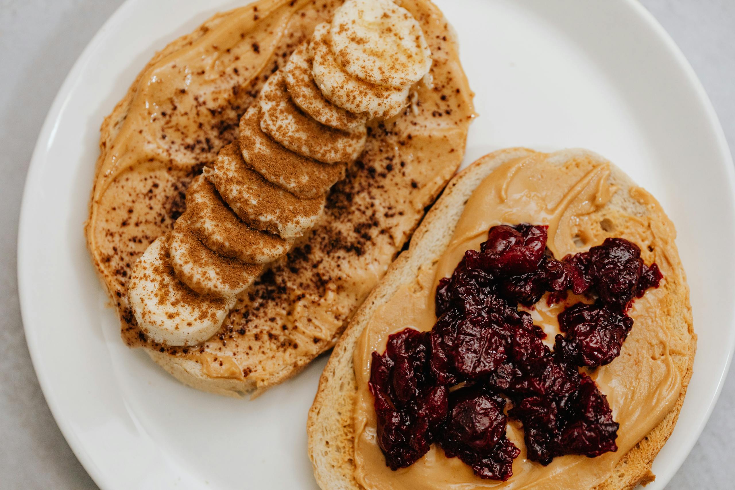 Close-up of peanut butter toast with banana and jam toppings on a plate.