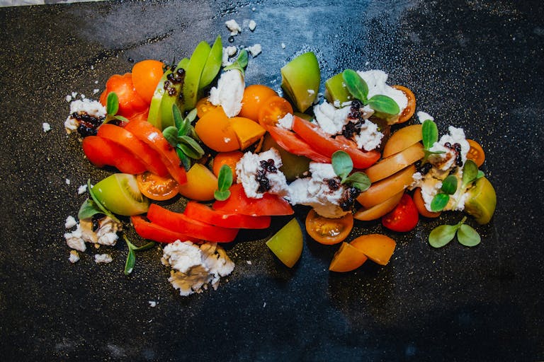 Colorful tomato salad with cheese and greens on a dark slate background.