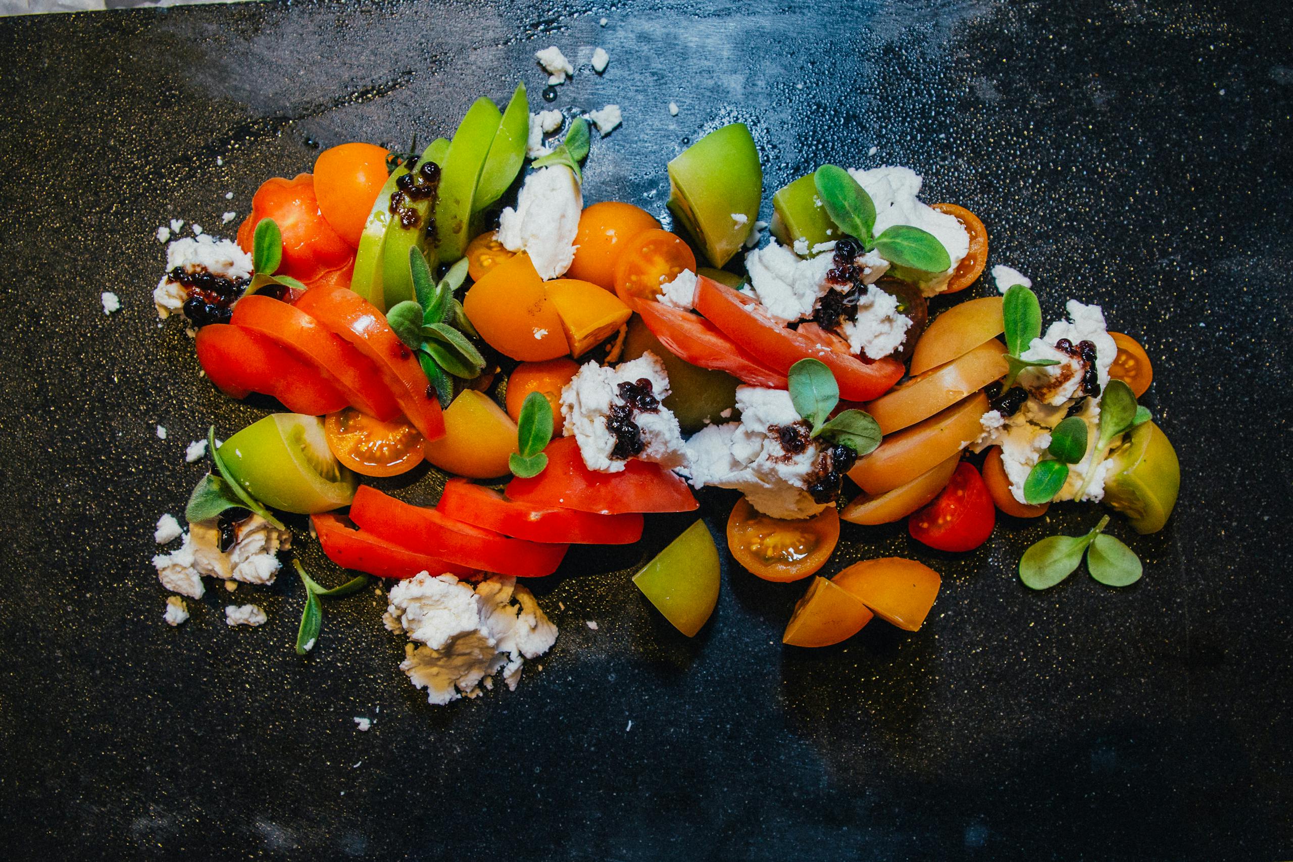 Colorful tomato salad with cheese and greens on a dark slate background.