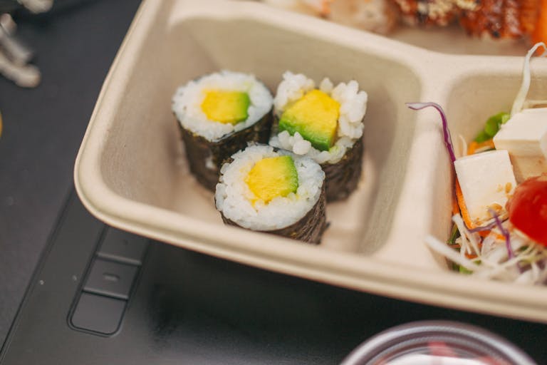 Delicious close-up of sushi rolls and fresh salad in a bento box, ideal for healthy eating.
