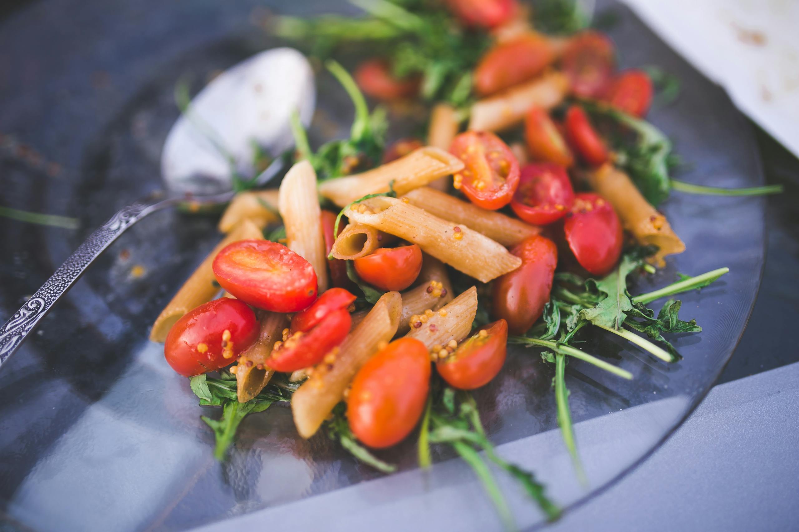 Fresh penne pasta salad with cherry tomatoes and arugula on a glass plate.