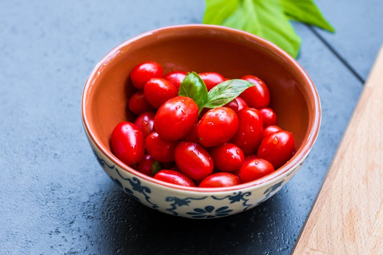 Juicy cherry tomatoes in a bowl with basil leaves, showcasing fresh and healthy ingredients.